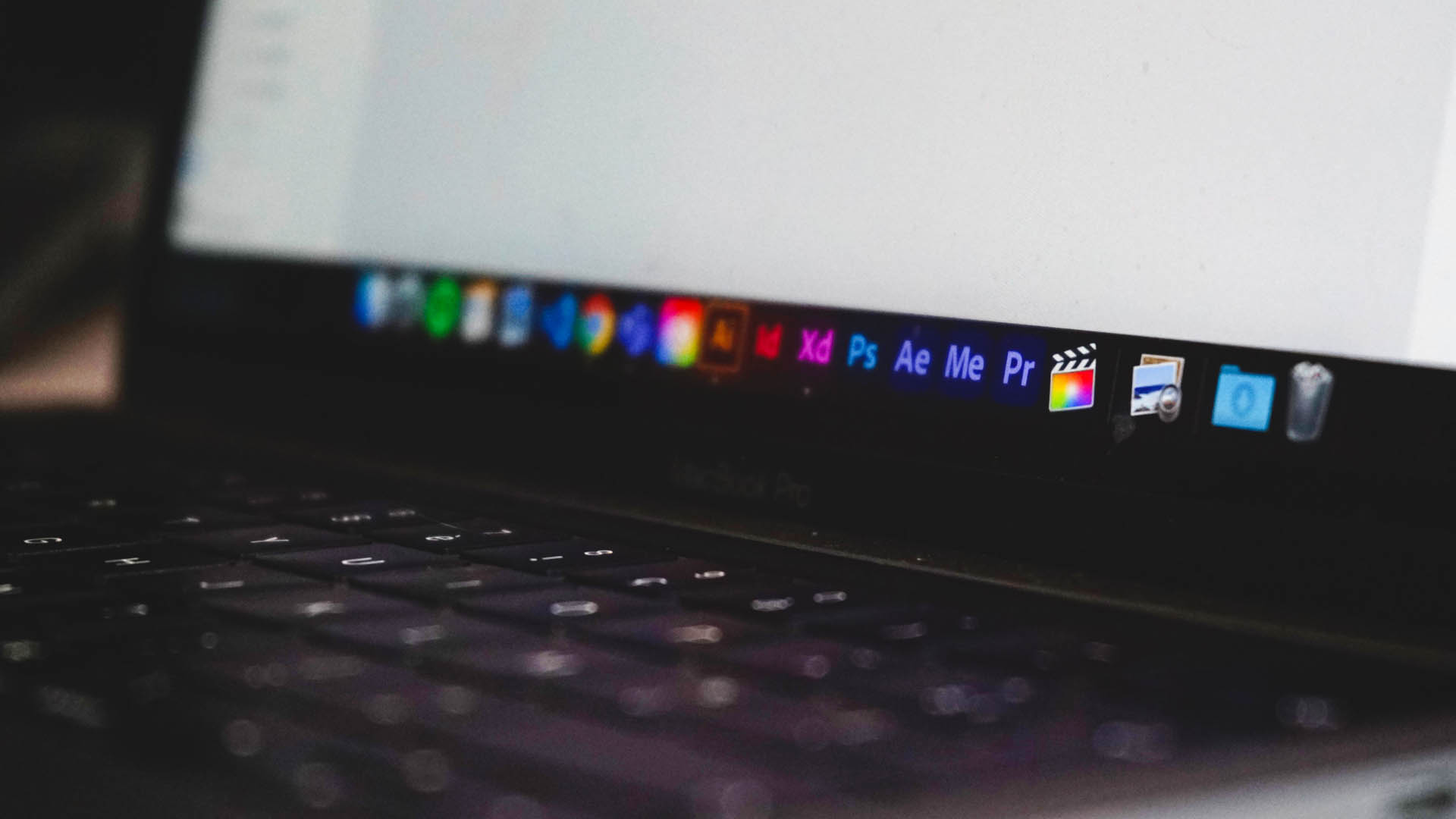 A photograph of a MacBook Pro laptop with the Adobe Creative Cloud Suite and Final Cut Pro in the menu on the screen