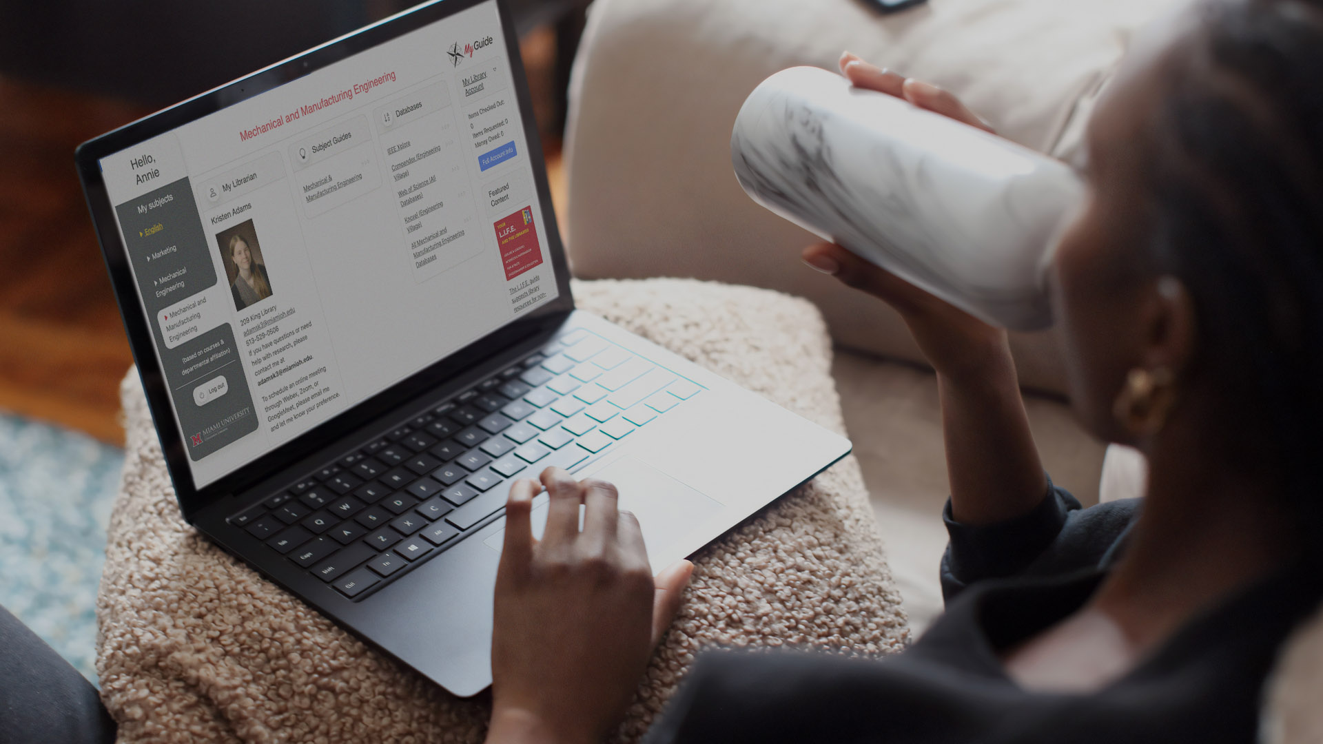 A Black woman drinks from a water bottle while using a laptop with MyGuide displayed on the screen.